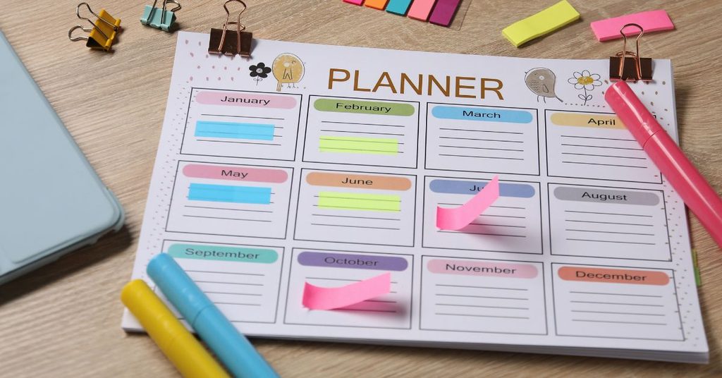 A colorful yearly planner with sticky notes, binder clips, and highlighters on a wooden desk