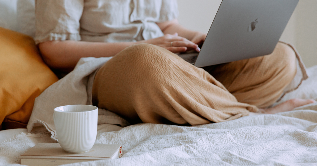 Woman relaxing on a bed with a laptop and a mug after using AI to organize her life