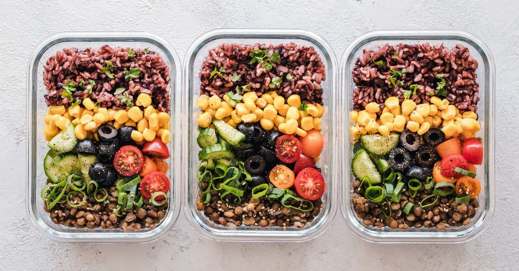 How to meal prep salads: three glass containers filled with rice, corn, cucumber, cherry tomatoes, olives and lentils