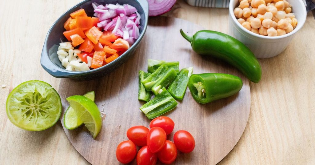 Chopped bell peppers, red onion, garlic and cherry tomatoes on a wooden cutting board