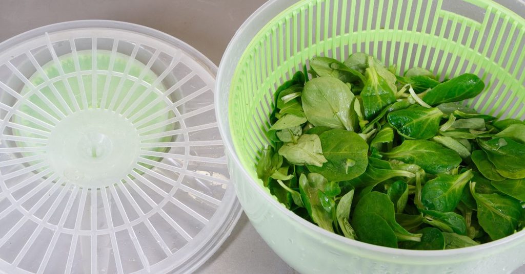 Freshly washed greens in a salad spinner basket next to its lid