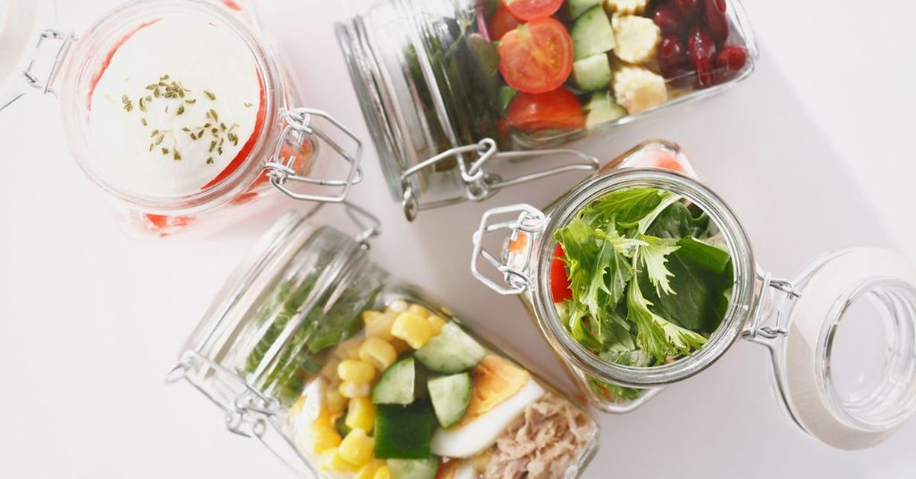 Layered salads in clip-top glass jars with greens, tomatoes, cucumber, corn and egg