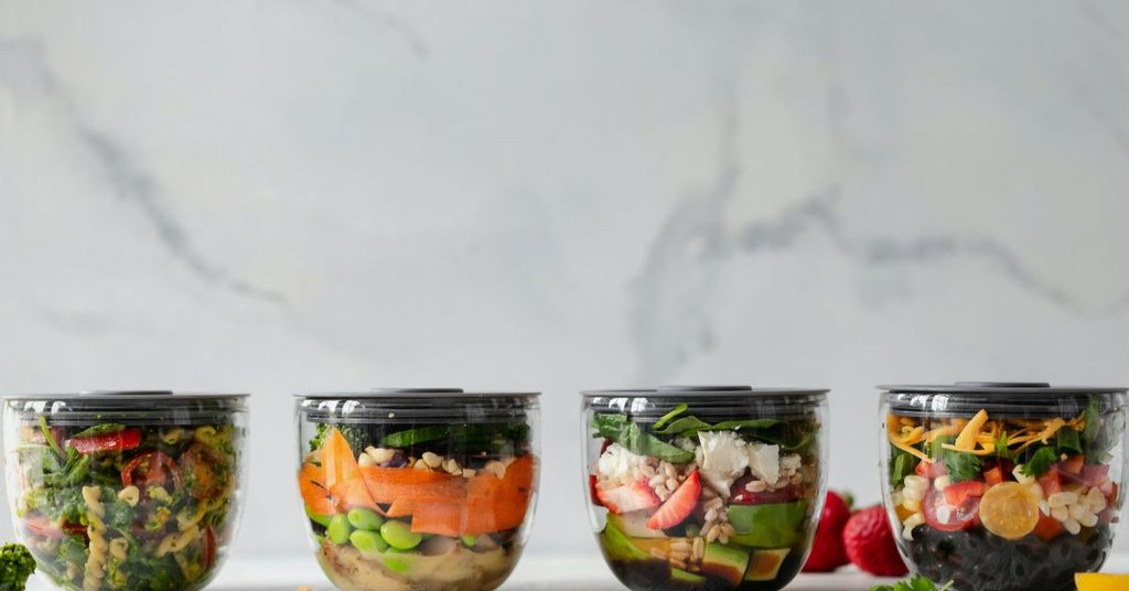 Four prepped salads in lidded containers on a marble counter, ready for the week after learning how to meal prep salads